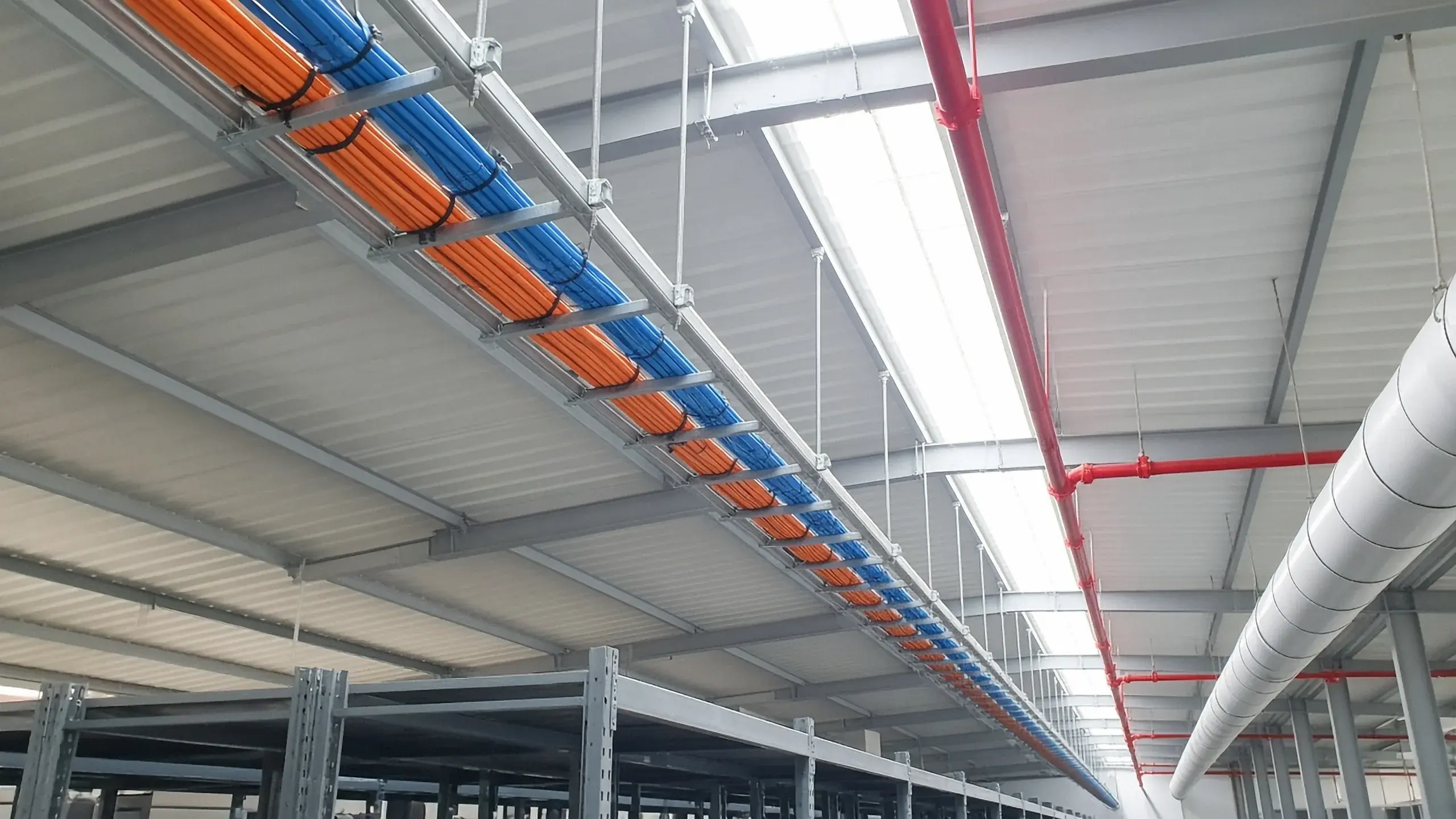 Kabelladder met oranje en blauwe kabelbundels onder het dak van een distributiecentrum